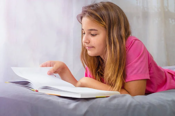 Genç kız yatak odasındaki yatakta kitap okuyor.
