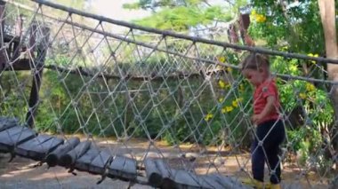 Kız ekolojik bir oyun parkında asma köprü boyunca yürüyor