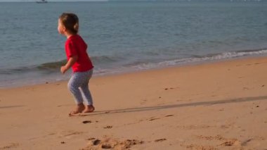 Mutlu kız çocuğu tatilde sahilde koşuyor.