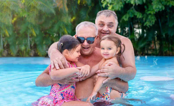 Portrait of grandfather and great-grandfather with children in the pool on vacation