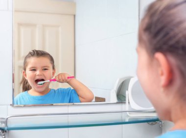 Dişlerini fırçalayan kız tuvaletteki aynaya bakıyor.