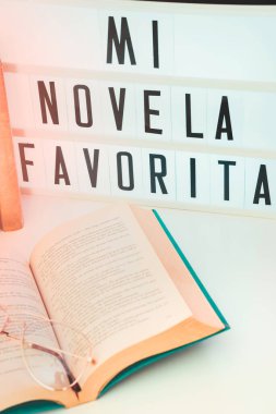 Yakın plan. Uluslararası Kitap Günü 'nün mesajlı olduğu ışık kutusu, yanında kitap ve yatak odasındaki komodinin üzerinde bir çift gözlük bulunan açık bir kitap..
