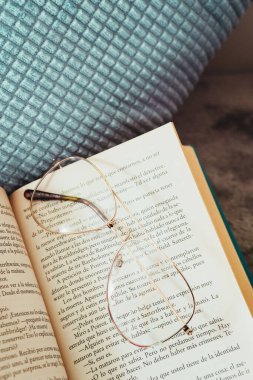 Yakından çekelim. Bardaklar açık kitap üzerinde dinleniyor, yatak odasındaki yastığın yanında, sabah.