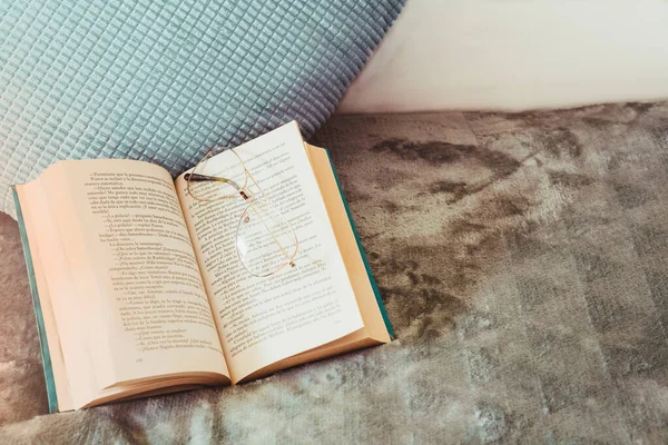 Orta düzlem. Bardaklar açık kitap üzerinde dinleniyor, yatak odasındaki yastığın yanında, sabah.