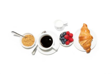 Güne güçle başlamak için tam bir kahvaltı. İçinde ahududu, yabanmersini, bir sürahi sütlü kahve, panela (tatlı ekmek) ve kruvasan bulunur..