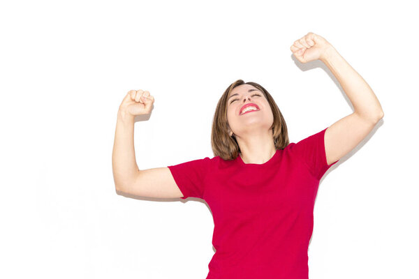 Image of a young woman celebrating a victory, bob haircut and casual fuchsia T-shirt isolated on a white background.