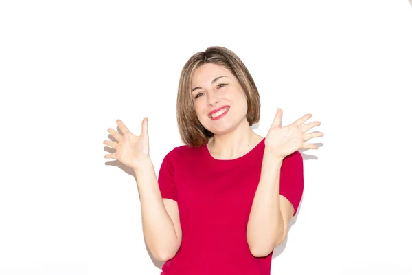 Beyaz arka planda el sallayarak gülümseyen mutlu beyaz bir kadının yatay görüntüsü. Bob saç kesimi, gerçek gözler ve sıradan fuşya tişörtü..