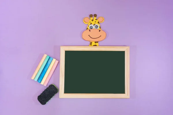 Mor arka planda, okul malzemeleriyle komik bir geçmişi var. Kara tahta, tebeşir, silgi ve çocuk yapımı Eva plastik zürafa. Metin için boşluk.