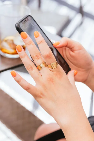 Açık tenli, turuncu parmaklı ve tırnaklı genç bir kadının elleri cep telefonuyla internet başvurusu yapıyor, internette geziniyor, sosyal medyada sohbet ediyor, elinde cep telefonu tutuyor..
