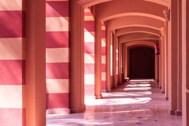 Terracotta koridoru ve zıt güneş ışığı kemerleri.