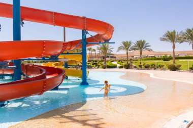 Hurghada, Kızıldeniz Valiliği, Mısır 17.09.2021: Küçük kız renkli su kaydıraklarının yanındaki su parkının ortasında duruyor
