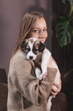 Kız kucağında küçük beyaz bir köpek yavrusu tutuyor ve ona sarılıyor.