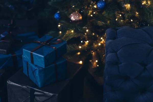 ガーランドライト付きクリスマスツリーの下に弓と贈り物と青い箱があります — ストック写真