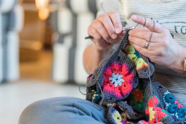 Bir kadın yerde lotus pozisyonunda oturur ve çiçek desenli açık ekose örer..