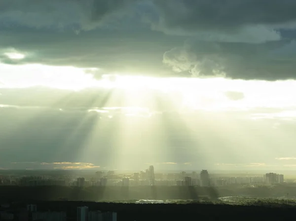 Batan güneşin fantastik parlak ışınlarının manzara görüntüsü yoğun bulutların arasından kırılıyor ve şehir binalarını aydınlatıyor.