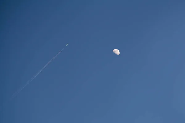 Uçak uçar ve akşam gökyüzünde beyaz bir iz bırakır. Ay 'ın arka planına karşı. Yaklaş.