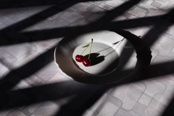 Masada beyaz bir tabakta iki kiraz, beyaz bir masa örtüsüyle örtülmüş, örgü gölgesi olan, yaklaş.