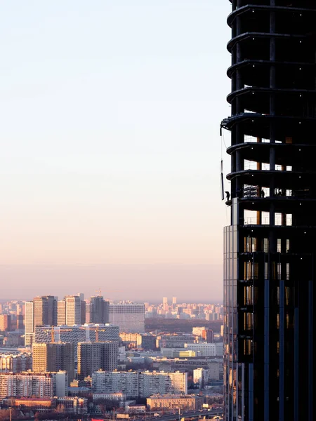 Birkaç inşaatçı, şehrin ve gökyüzünün arka planına karşı inşa halindeki bir gökdelenin üst katına çift camlı bir pencere kuruyor.