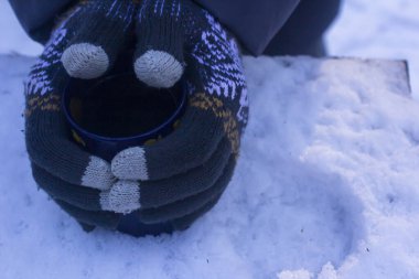 Eldivenli çocuk kışın çaylı bir kupayla ellerini ısıtır.