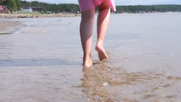 En flicka går barfota på sanden. Vatten kommer till stranden, en flicka hoppar på vågorna. — Stockvideo