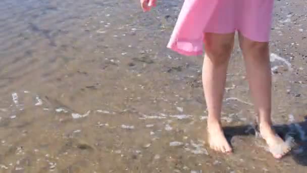 En flicka går barfota på sanden. Vatten kommer till stranden, en flicka hoppar på vågorna. — Stockvideo