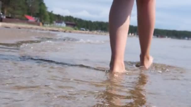 En flicka går barfota på sanden. Vatten kommer till stranden, en flicka hoppar på vågorna. — Stockvideo