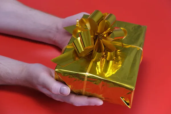 Mãos masculinas close-up em um fundo vermelho.Homem segura uma caixa com um presente em sua mão. Conceito para o Natal, Ano Novo 2022, Black Friday. — Fotografia de Stock