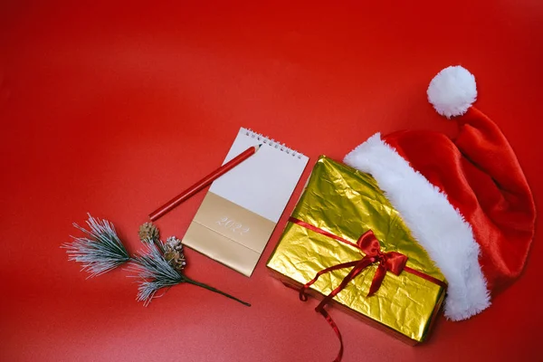 Świąteczne zakupy. Lista zakupów i prezentów na nowy rok. Santa Claus kapelusz leży na złotym polu na czerwonym tle. — Zdjęcie stockowe