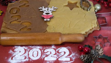 Kırmızı zemin üzerinde ahşap bir tahtada ev yapımı zencefilli kurabiye yapmak için Hamur. Noel ve Yeni Yıl 2022 konsepti. Seçici odak