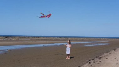 Beyaz Deniz kıyısında uçurtmayla oynayan bir kız. Mavi gökyüzüne karşı çok renkli bir uçurtma..