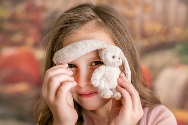 Pembe elbiseli bir kızın portresi, elinde oyuncak bir tavşan, kulağının altından gözetliyor. Karanlık arka plan. Seçici odak.