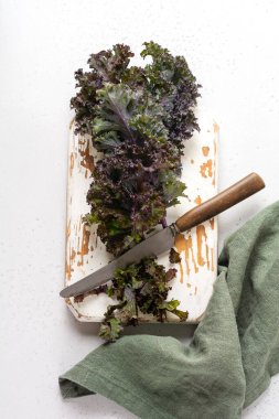 Kale açık gri kayrak, taş ya da beton zemin üzerinde kesme tahtasına taze yeşil kıvırcık bırakır. Seçici odaklanma. Sağlıklı vejetaryen yemekleri.