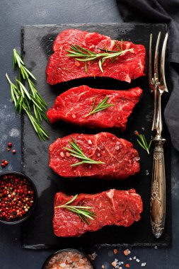 New York usulü iki çiğ biftek, biberiye ve baharatlı parşömen kağıdının üzerinde eski, siyah taştan bir arka plan. Üst Manzara. Model.