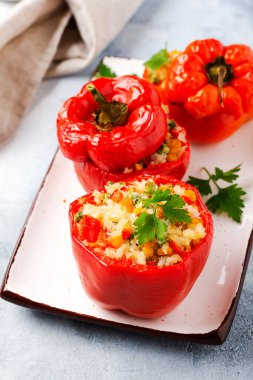 Pirinç ve sebzeyle doldurulmuş kırmızı dolma biberler gri beton arka planda dökme demir tavada.