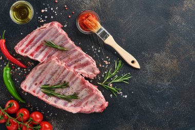 Çiğ domuz kaburgası ya da baharatlı, siyah ahşap tepside kırmızı biber, sarımsak karanfili ve otlu taze et. Metin için kopyalama alanı olan koyu dokulu arkaplan.
