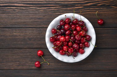 Koyu kahverengi taş masadaki beyaz kâseye su damlatılan kiraz. Taze kirazlar. Tatlı kırmızı kirazlar. Üst Manzara. Kırsal tarzda. Meyve Arkaplanı