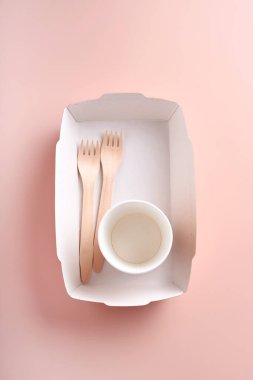 Kağıt bardaklar, çanaklar, torbalar, tahta çatallar, içme kamışları, fast food kapları, pembe arka planda ahşap çatal bıçaklar. Eko kağıt sofra takımı. Geri dönüşüm ve gıda teslimatı konsepti. Model yap. Üst görünüm