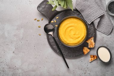 Balkabağı geleneksel çorbası kremalı ipeksi desenli adaçayı ve siyah tabakta kırmızı biber. Eski gri arka plan. Uzayı kopyala Model yap. Üst manzara, düz uzanma.