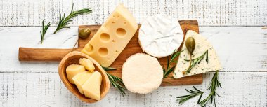 Set ya da çeşitli peynirler. Baharatlı suluguni, camembert, mavi peynir, parmesan, maasdam, biberiyeli brie peyniri ve biber. Beyaz ahşap arka planda. Üst Manzara. Uzayı kopyala Pankart.