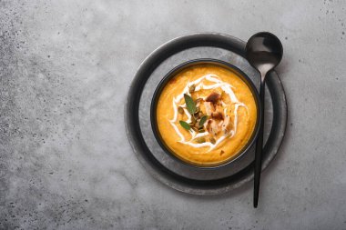 Balkabağı geleneksel çorbası kremalı ipeksi desenli adaçayı ve siyah tabakta kırmızı biber. Eski gri arka plan. Uzayı kopyala Model yap. Üst manzara, düz uzanma.