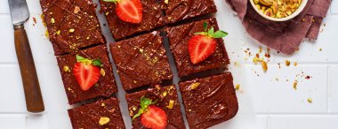 Fıstıklı çikolatalı kareler ve beyaz arkaplanda beyaz kağıt üzerinde çilek, üst manzara, yatay kompozisyon. Düz yiyecek..