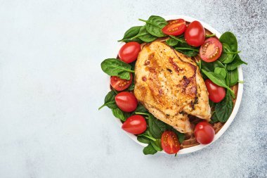 Izgara tavuk göğsü, ıspanak yeşili salata, biber ve kiraz domatesleri beyaz masa arkasında seramik tabakta. Sağlıklı yiyecekler, ketojenik diyet, öğle yemeği konsepti. Üst Görünüm ve Uzayı Kopyala