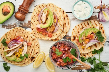 Izgara tavuk, avokado, mısır taneleri, domates, soğan, kişniş ve salsa soslu beyaz ahşap masa. Geleneksel Meksika ve Latin Amerika sokak yemekleri. Üst görünüm.