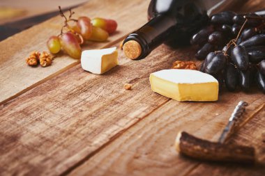 Tirbuşonlu bir şişe şarap. Üzümlü, peynirli Camembert dilimli, eski gri beton masa arkaplanlı ve fotokopi alanı olan. Asma dallı kırmızı şarap. Kırsal arka planda şarap kompozisyonu. Model.