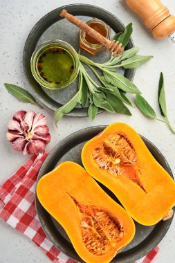 Yarım parça çiğ organik tereyağlı kabak, adaçayı yaprağı, çok renkli sarımsak, bal, tuz ve biber beyaz bir tahta, taş ya da beton arka planda. Yemek arkaplanı. Kopyalama alanı olan üst görünüm.