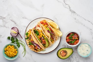 Beyaz taş masada ızgara tavuk, avokado, mısır taneleri, domates, soğan, kişniş ve salsa soslu Meksika tacoları. Geleneksel Meksika ve Latin Amerika sokak yemekleri. Üst görünüm.