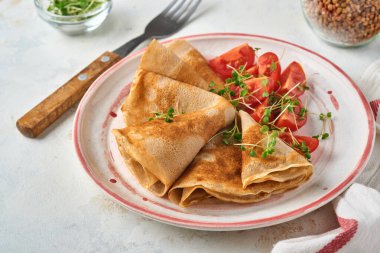 Glütensiz glütensiz karabuğday unu krep kiraz domatesli ve roka mikroyeşili beyaz tabakta, kahvaltı için ev yapımı sağlıklı pişirme. Model yap. Boşluğu kopyala.