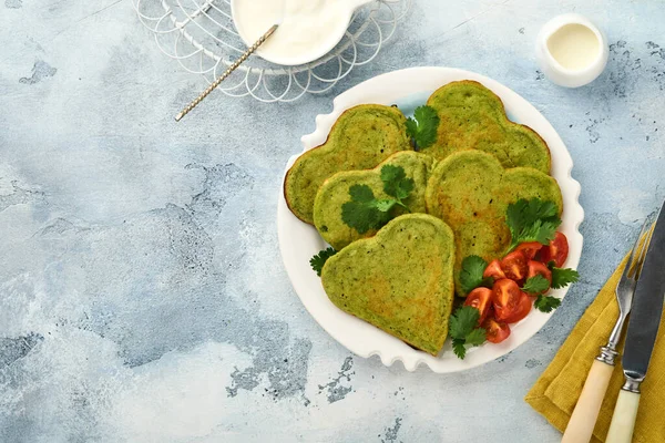 Crêpes à l'avocat aux épinards en forme de cœur avec sauce au yaourt grec et tomates cerises sur assiette blanche sur fond gris clair. Petit déjeuner concept de nourriture. Vue supérieure avec espace de copie. — Photo