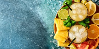 Taze meyve suyu ananası, buzlu ve çeşitli renkte tropikal meyve, portakal, limon, limon, düz konum, koyu mavi taştan arkaplan. Model.