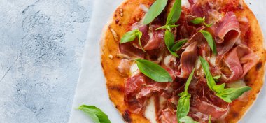 Jamonlu ev yapımı pizza, mozzarella ve arka planda taze fesleğen yaprakları. Üst görünüm.